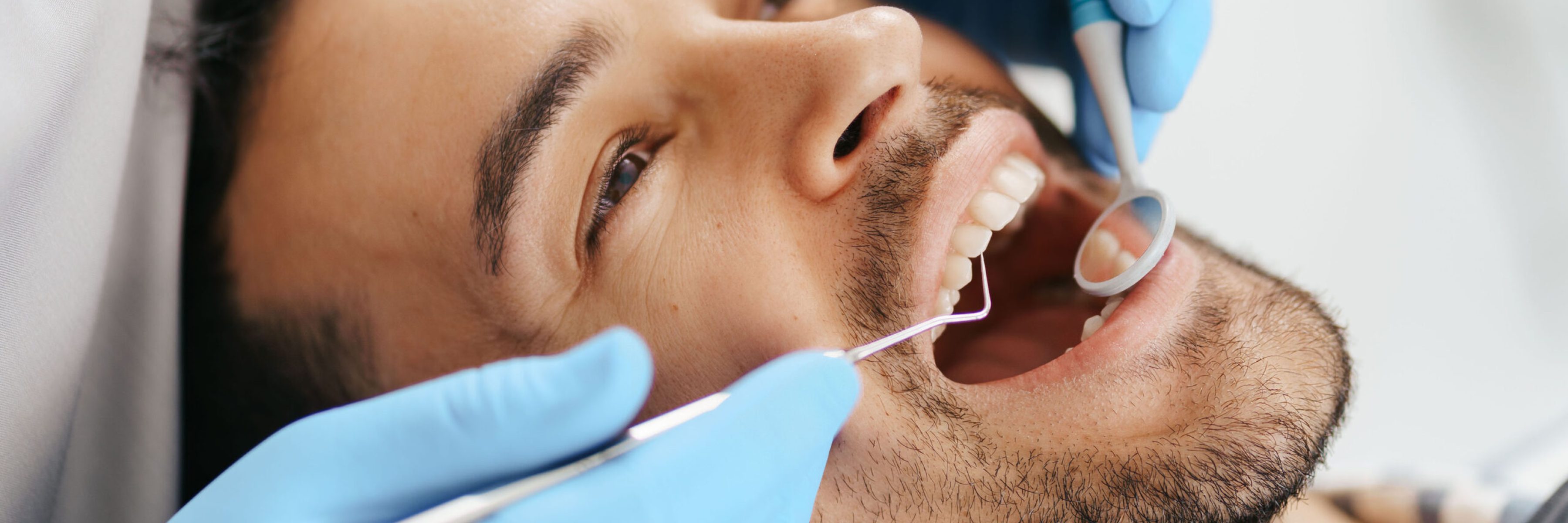Smiling young man sitting in dentist chair while doctor examining his teeth
