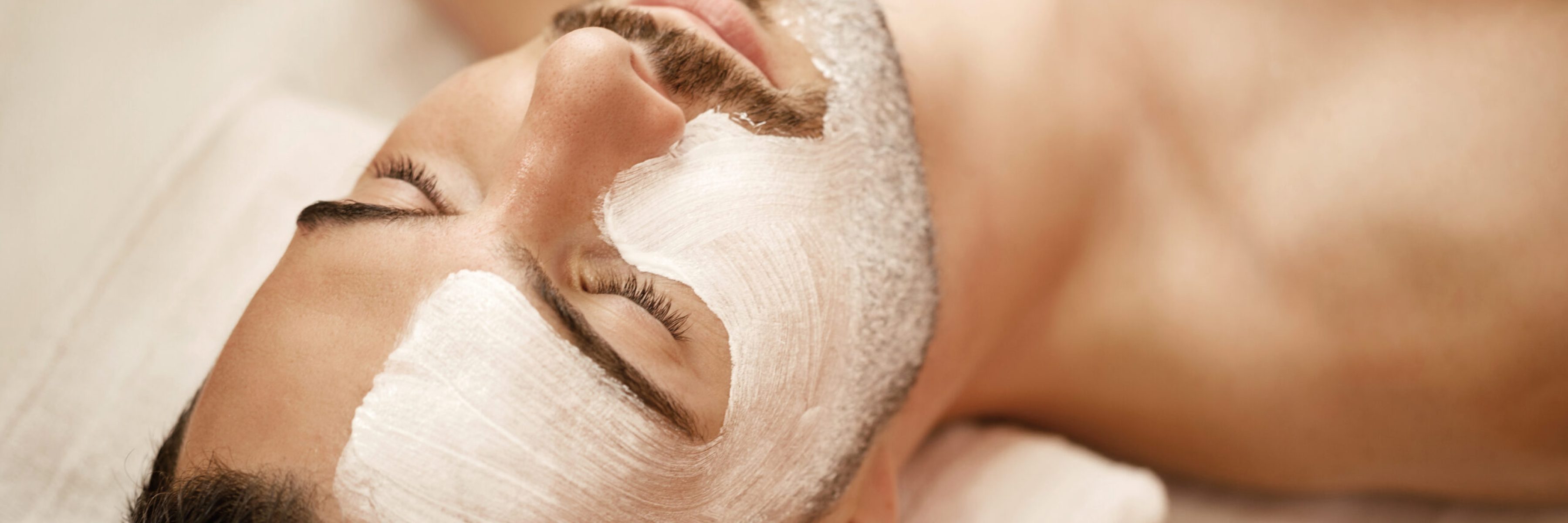 Close-up of man with white facial mask relaxing during treatment at beauty spa.